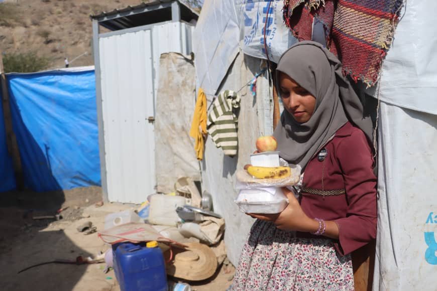 A woman carrying meals back to her tent